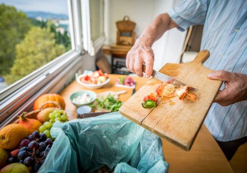 Persona cocinando con verduras frescas junto a un cubo de compost